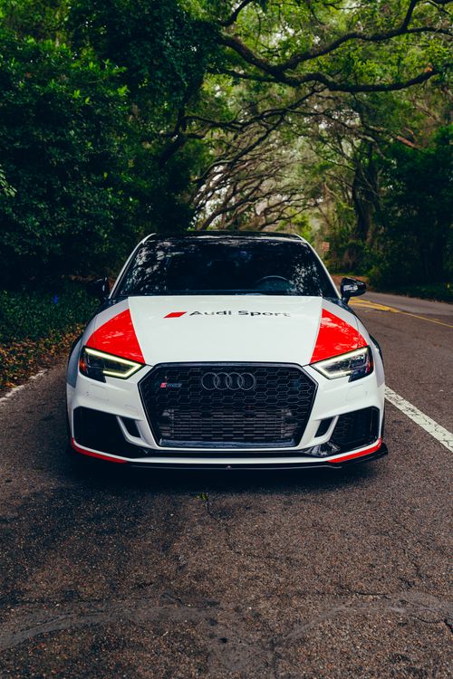 Free Front view of a sleek white sports car parked on a tree-lined road. Stock Photo