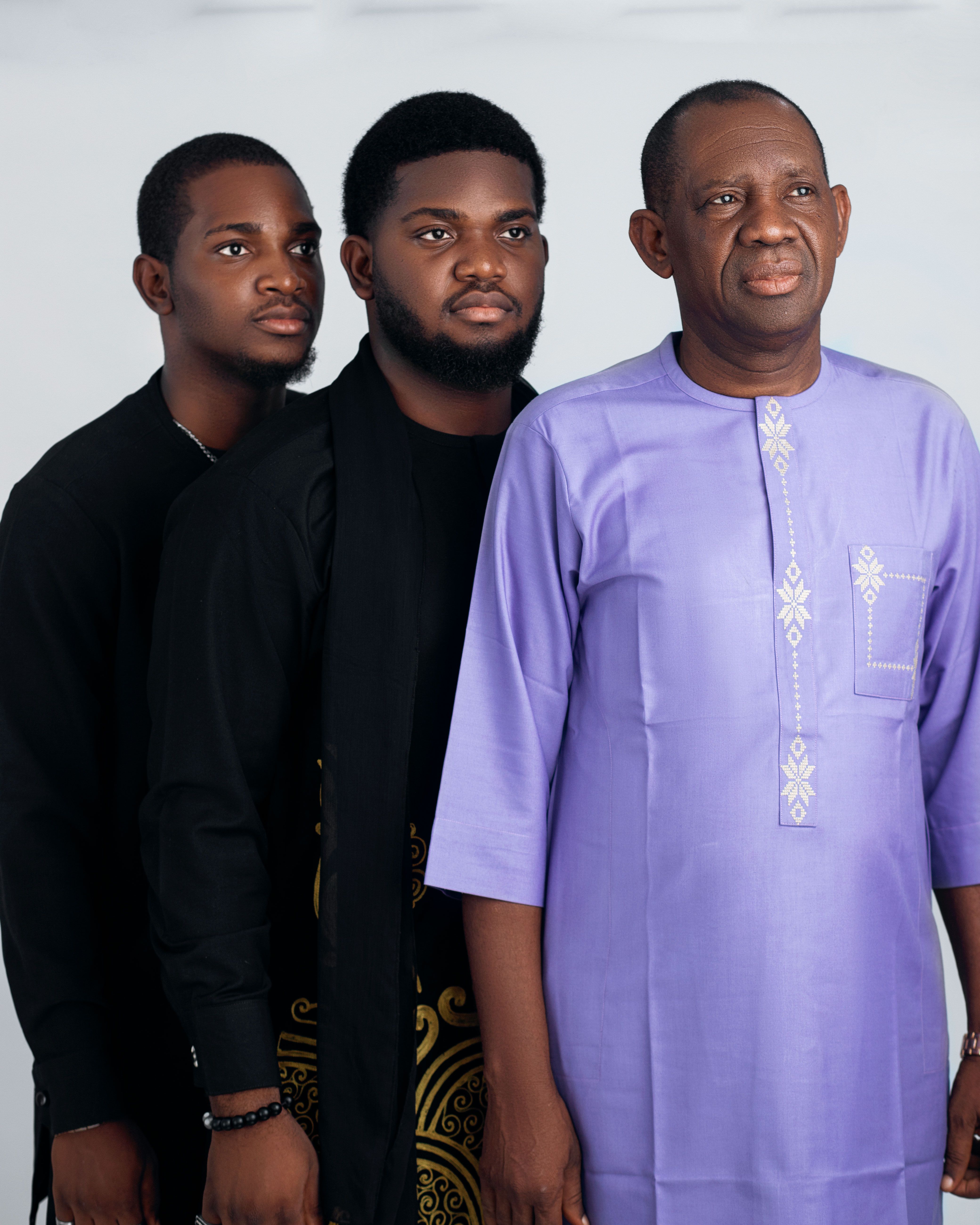 Three men standing in traditional African attire against a light background.
