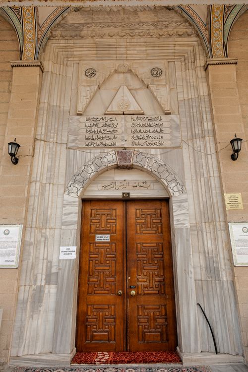 Free An intricately carved wooden door with Arabic inscriptions, framed by a marble archway. Ideal for cultural and architectural themes. Stock Photo