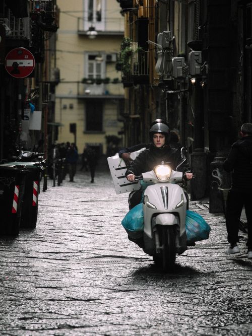 Free Scooter delivery in narrow city alleyway with cobblestone street and old buildings. Stock Photo