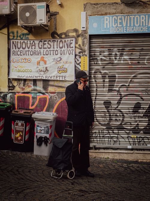 Free Man with shopping trolley talks on phone by a graffiti-covered wall in an urban scene. Stock Photo
