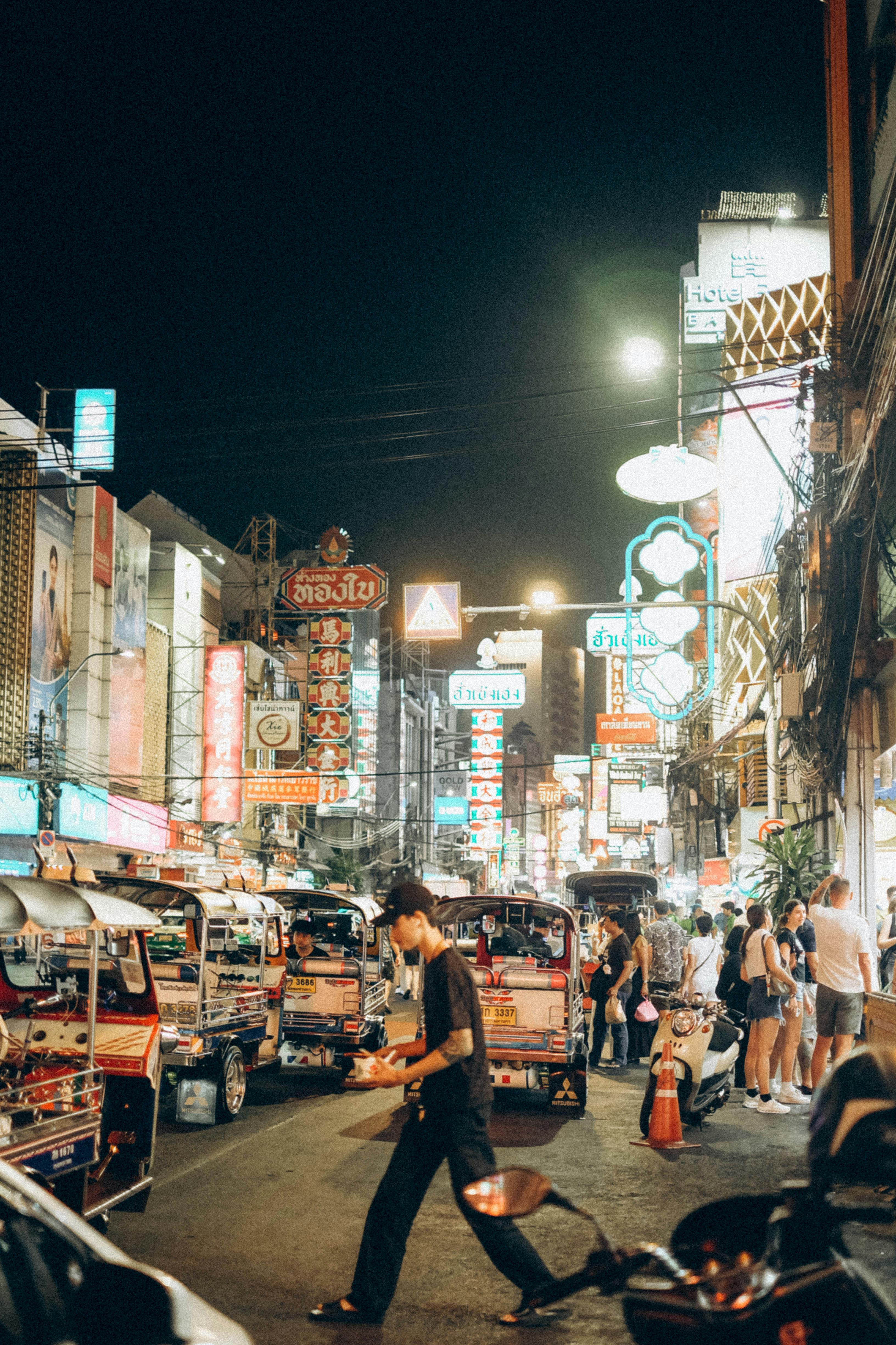 Explore the lively night scene in Bangkok's vibrant street filled with tuk-tuks and neon lights.