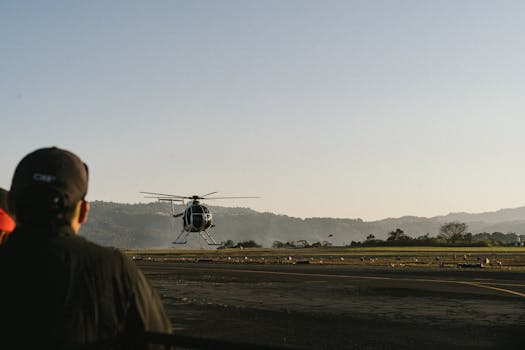 A helicopter takes off at Ilopango Airport in El Salvador, with mountains in the background.