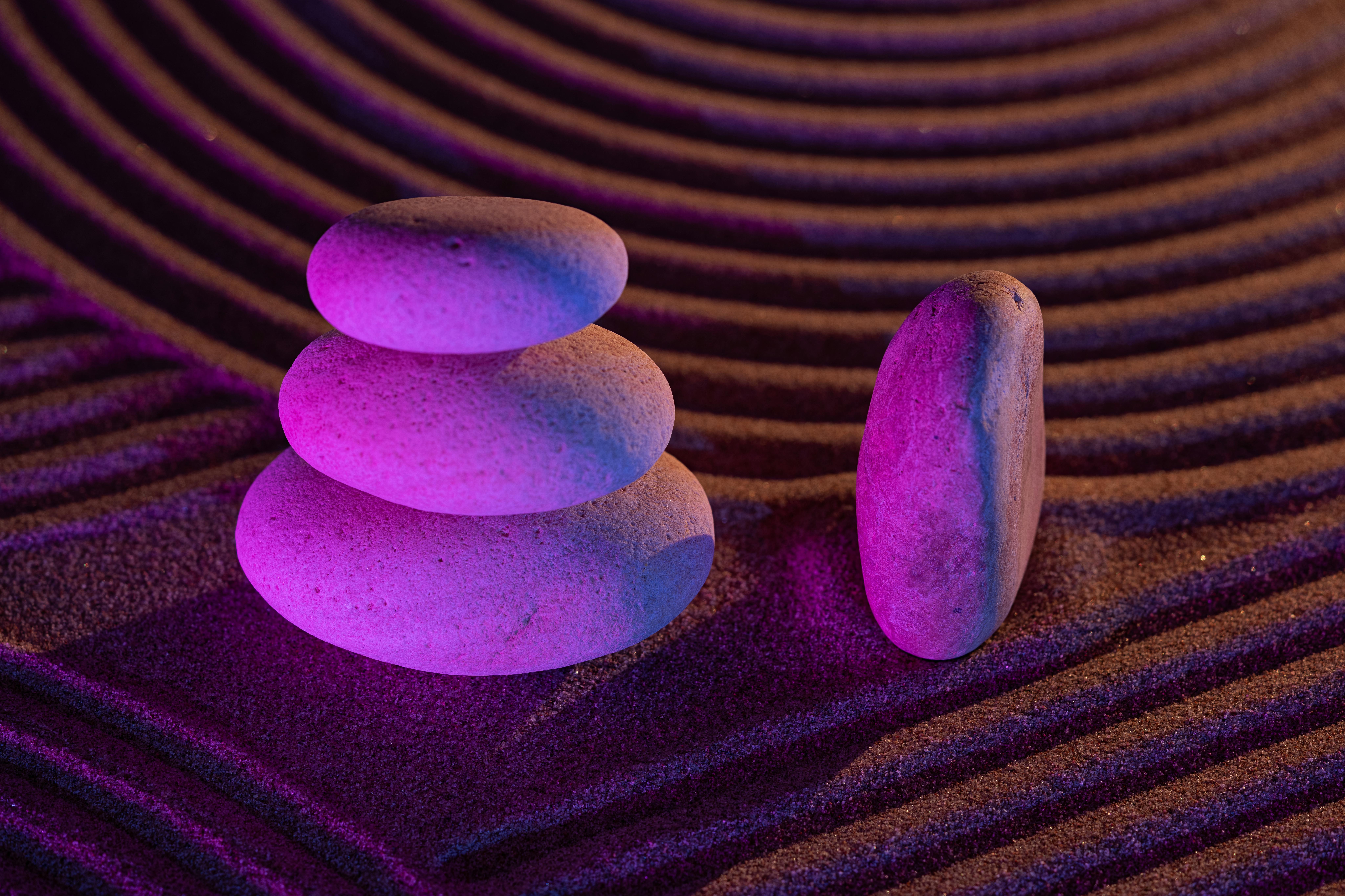 Gratis Tranquillo giardino zen con pietre impilate in una luce viola, circondate da motivi di sabbia che simboleggiano equilibrio e tranquillità. Foto a disposizione