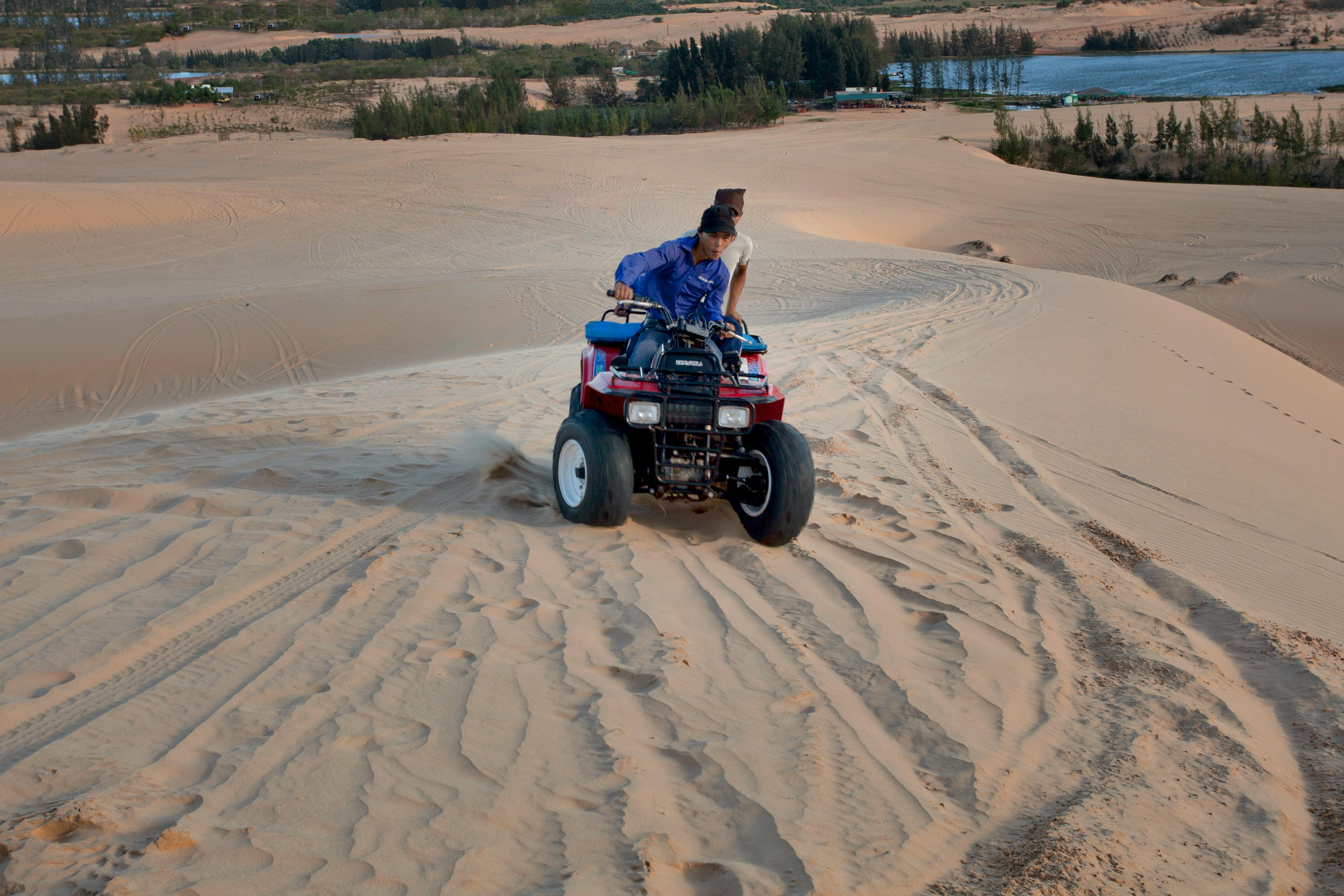 Two people riding an ATV through expansive sand dunes on a sunny day, perfect for adventurous travel