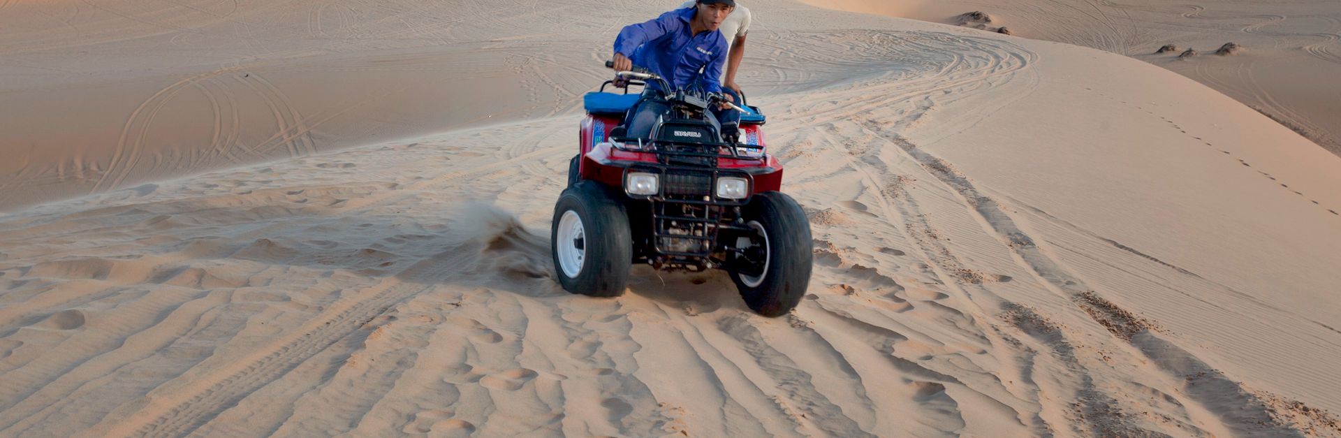 Two people riding an ATV through expansive sand dunes on a sunny day, perfect for adventurous travel