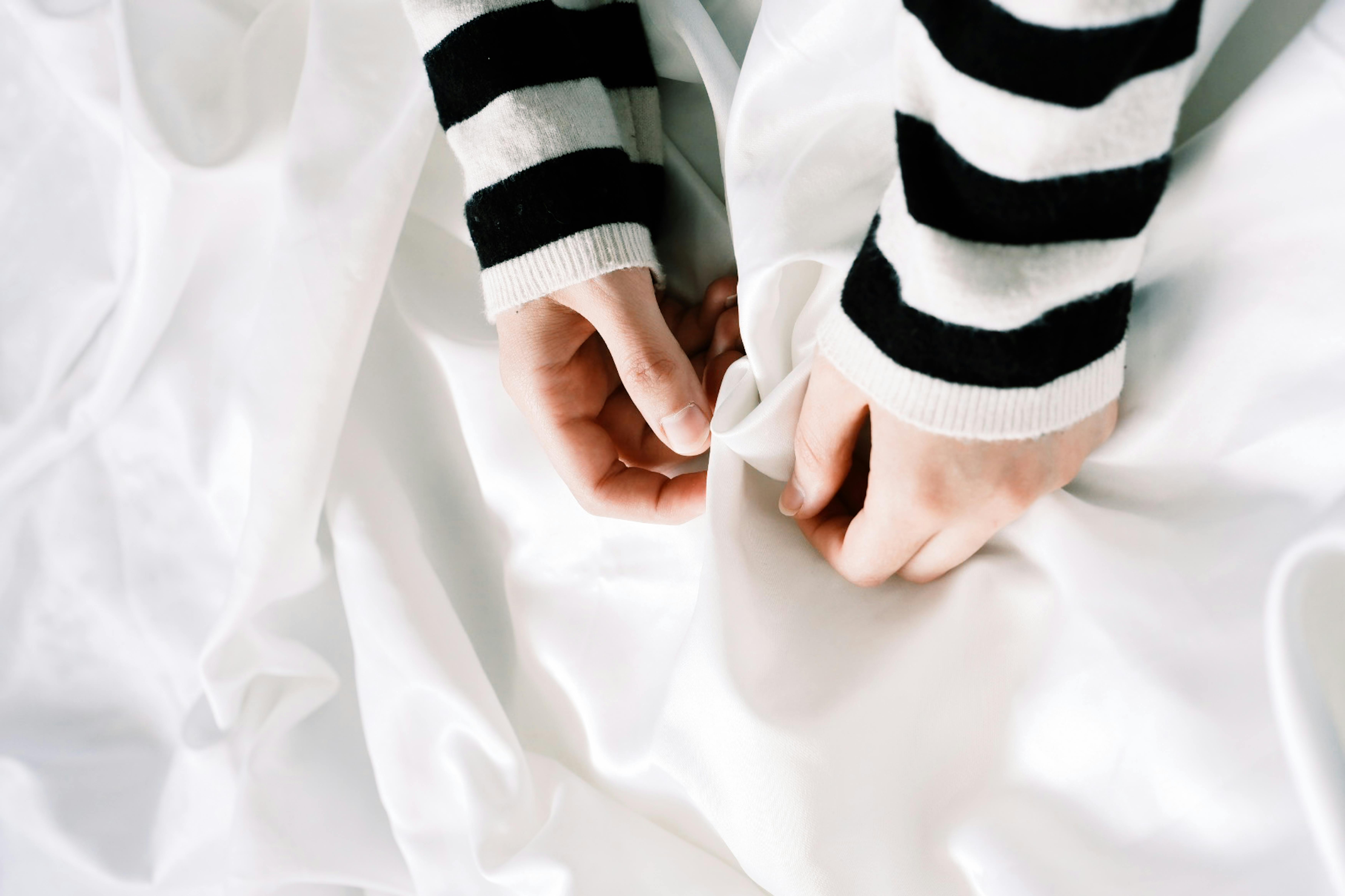 grátis Primeiro plano de mãos com mangas listradas segurando um tecido branco, transmitindo textura e minimalismo. Foto profissional