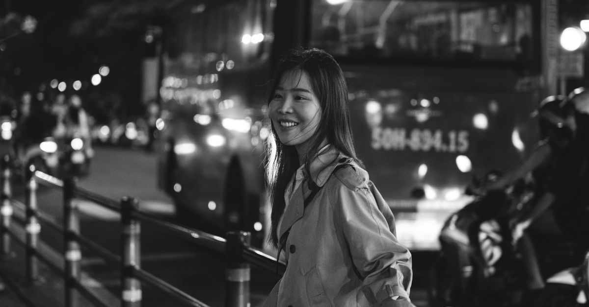 Uma mulher sorrindo em uma rua movimentada da cidade de Ho Chi Minh à noite, capturando a vibrante vida urbana.