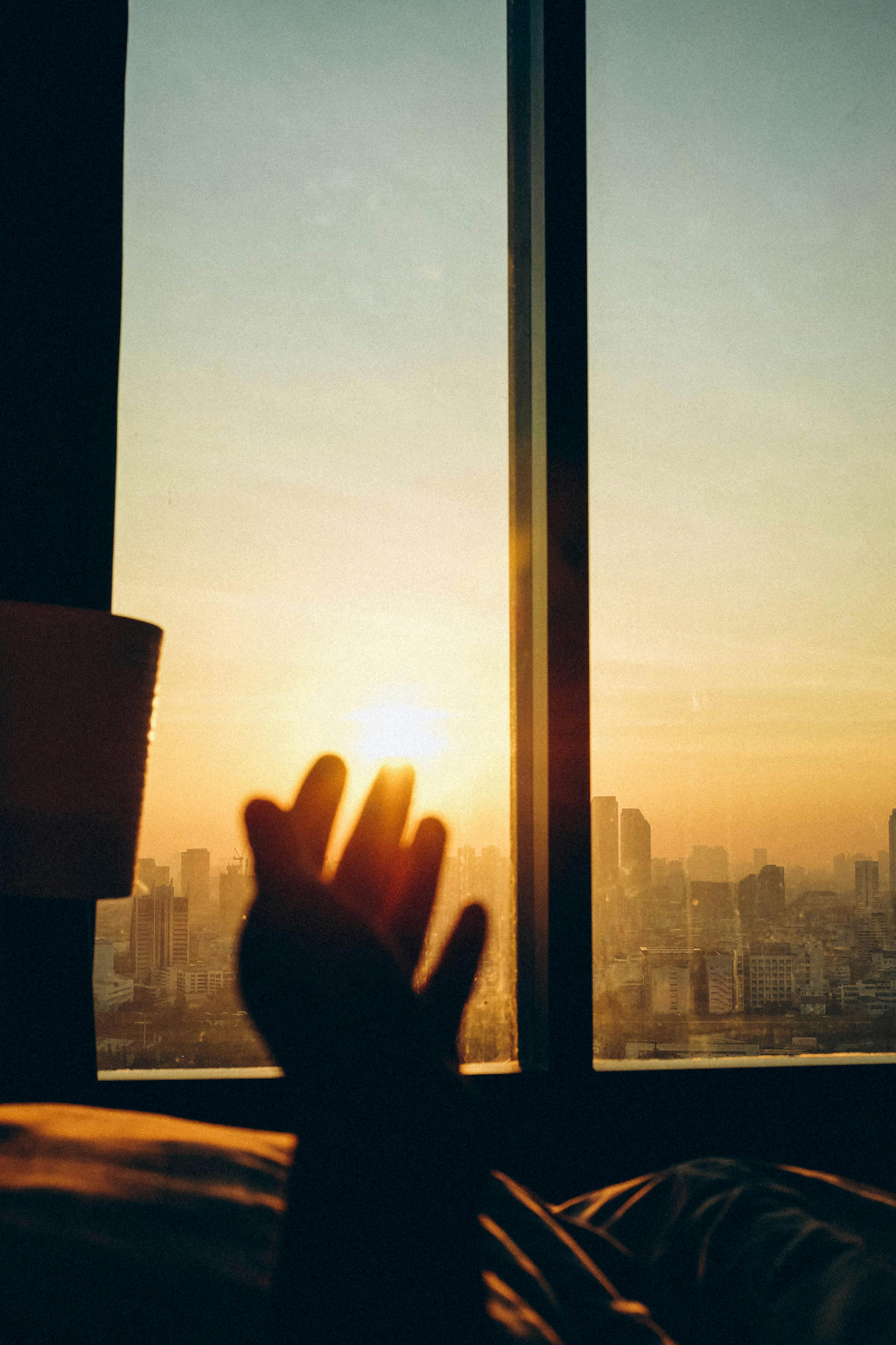 gratis Silhouet van een hand die naar de zonsopgang reikt boven de skyline van Bangkok. Stockfoto