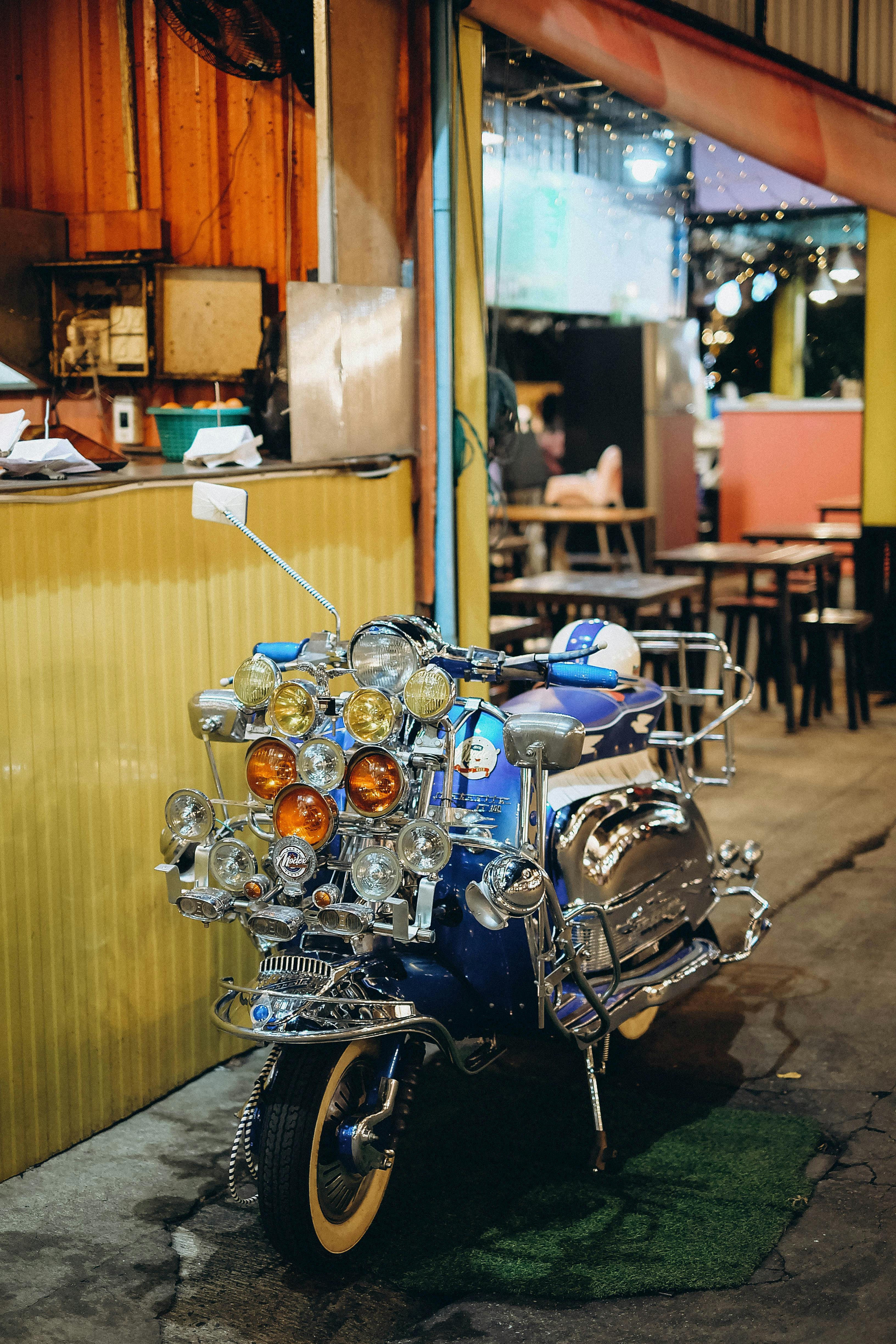 Free A heavily customized vintage scooter with multiple headlights parked near a vibrant Bangkok street. Stock Photo