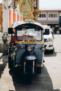 A vibrant tuk tuk parked on a sunny street in Bangkok with ornate temple in background.