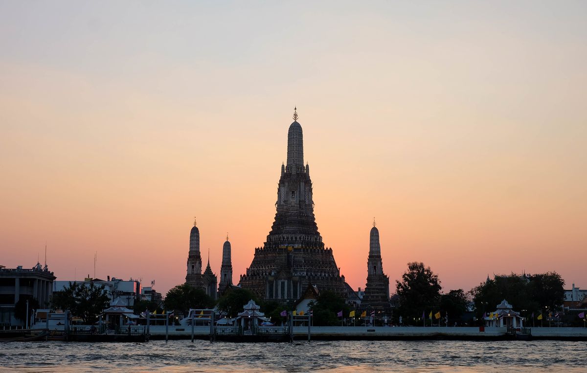 Wat Arun silhouetted at sunset — the Temple of Dawn's porcelain-encrusted prang rises 86 meters above the Chao Phraya.
