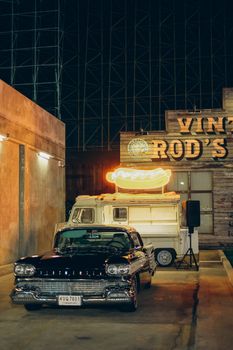 Classic car parked near a neon-lit food truck in Bangkok, Thailand, offering a retro ambiance.