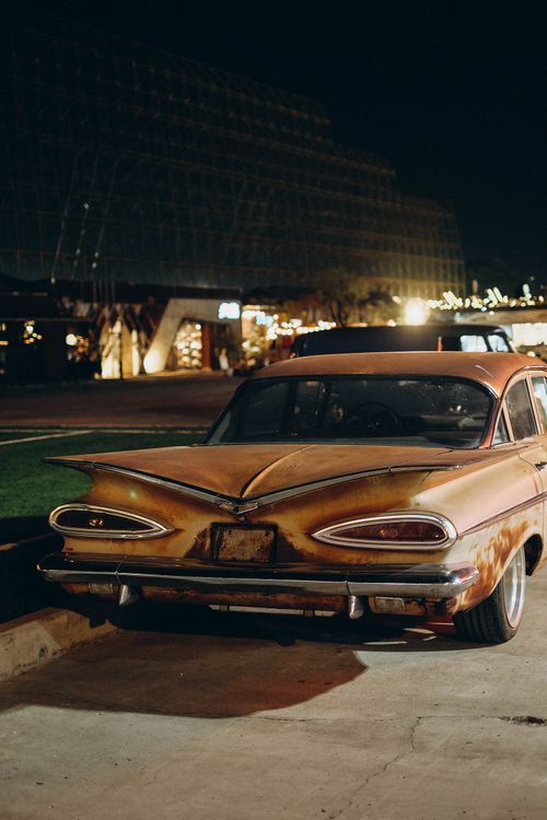Free Vintage car with rusted exterior parked at night in a lively Bangkok street. Stock Photo