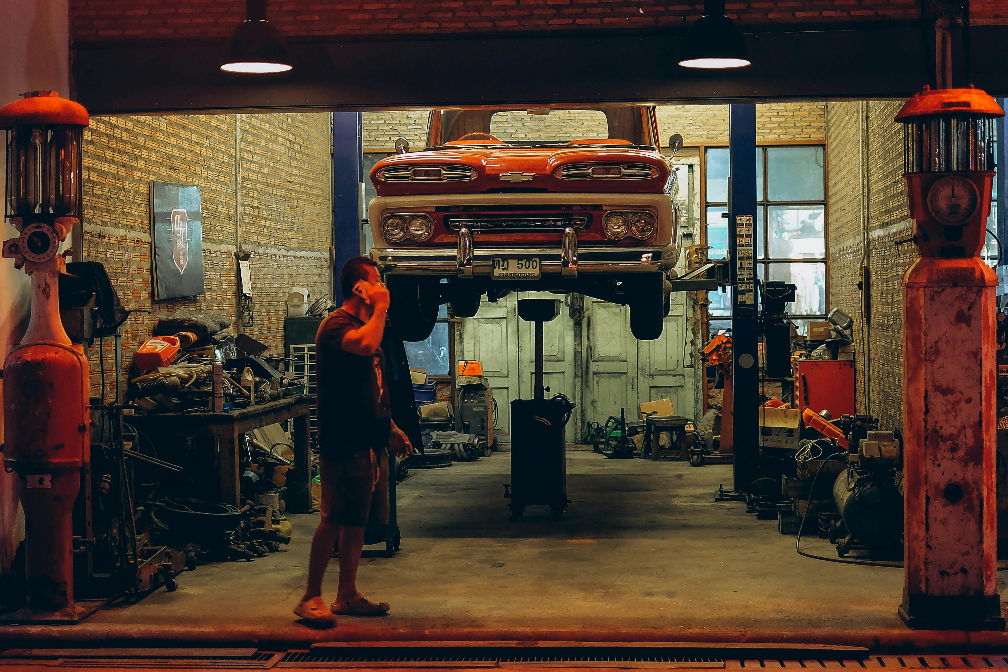 A red vintage truck is lifted in a Bangkok garage. Industrial setting with nostalgic automotive elements.