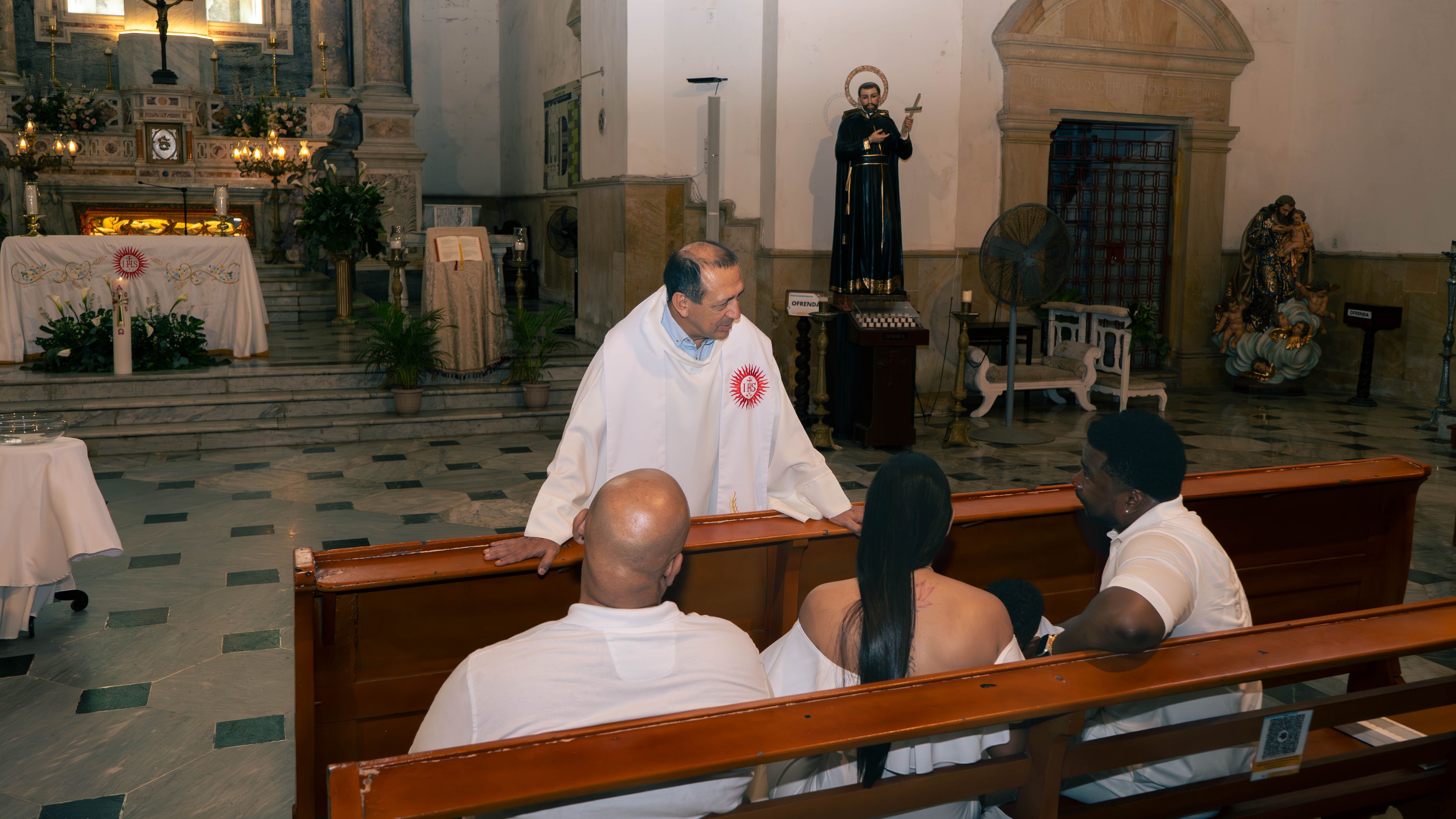 A priest converses with visitors inside a historic church setting, creating a warm and welcoming atmosphere.