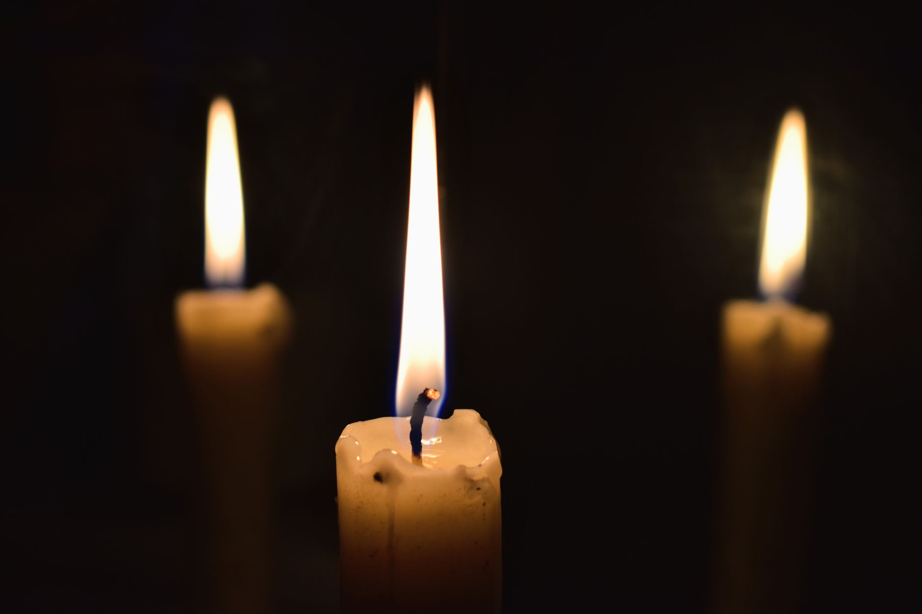 Three lit candles casting a warm glow in the darkness, creating a serene and contemplative atmosphere.