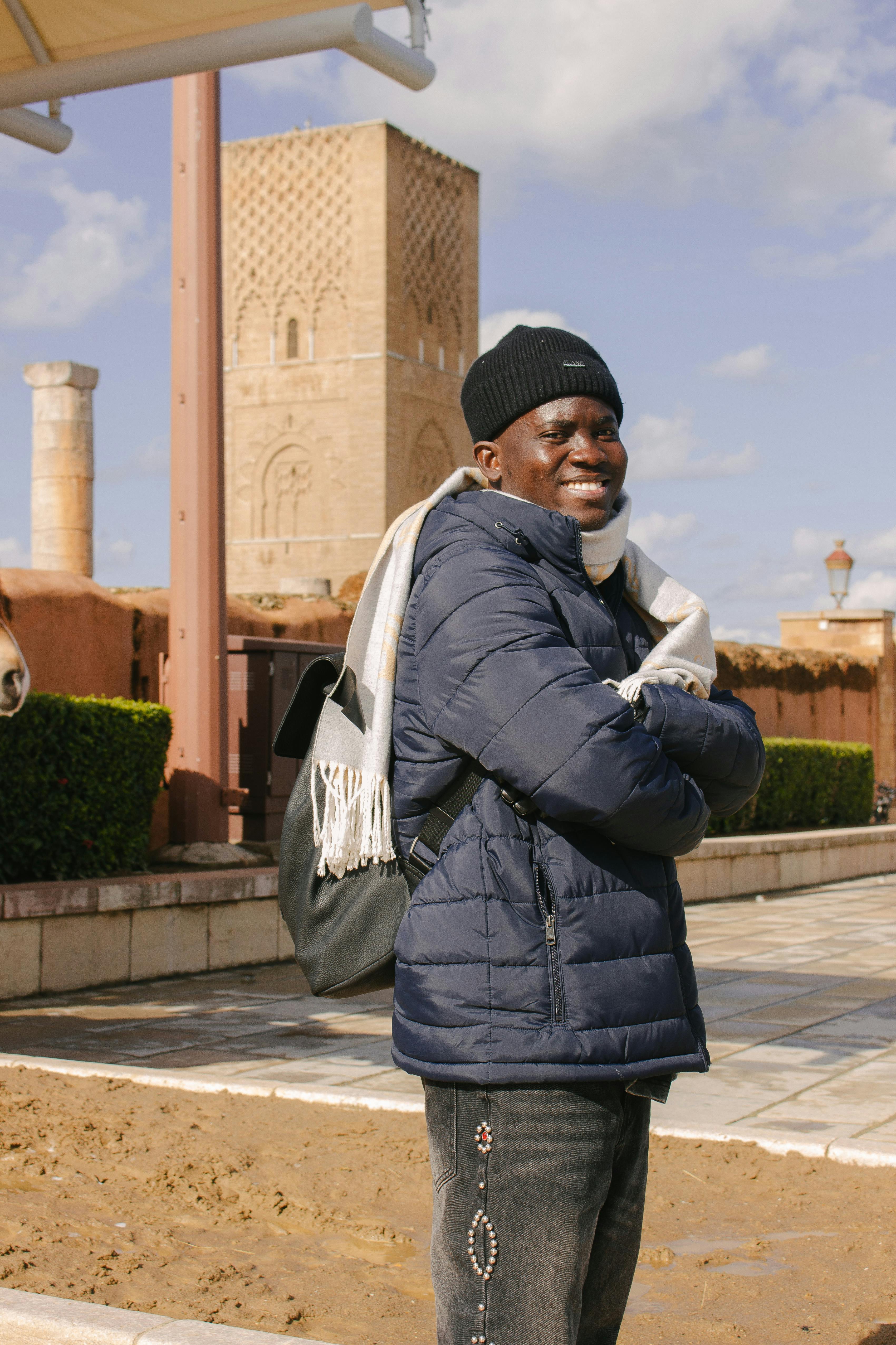 Smiling man in winter clothing in front of the iconic Hassan Tower in Rabat, Morocco.