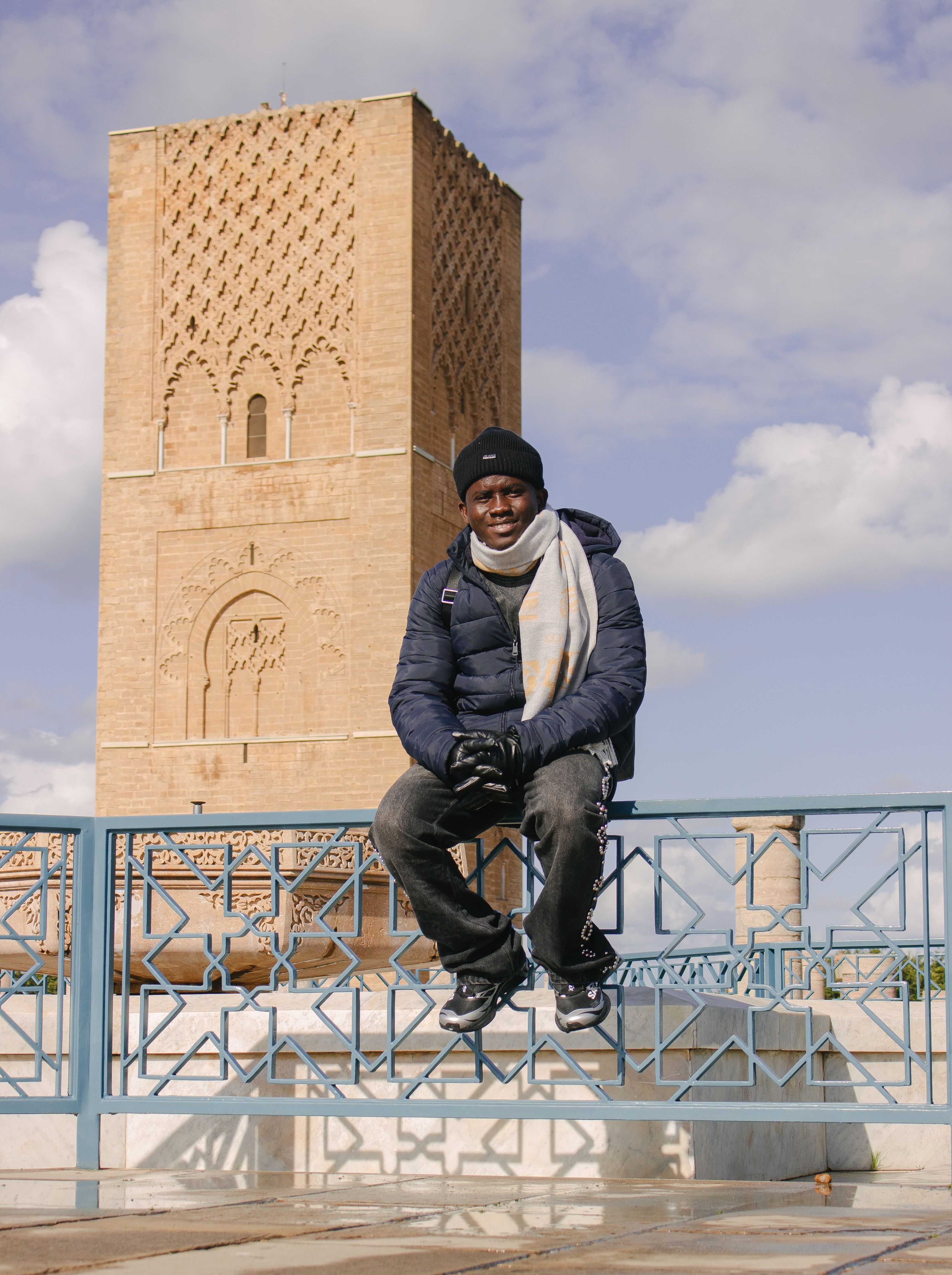 Man sitting on a railing by the iconic Hassan Tower in Rabat, Morocco.