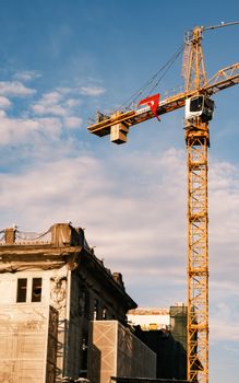 A construction crane near a historical building under blue sky with clouds.