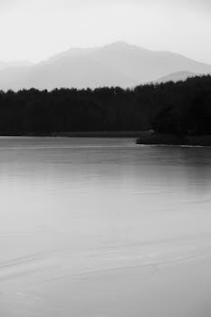 Serene black and white landscape of a tranquil lake with distant mountains.