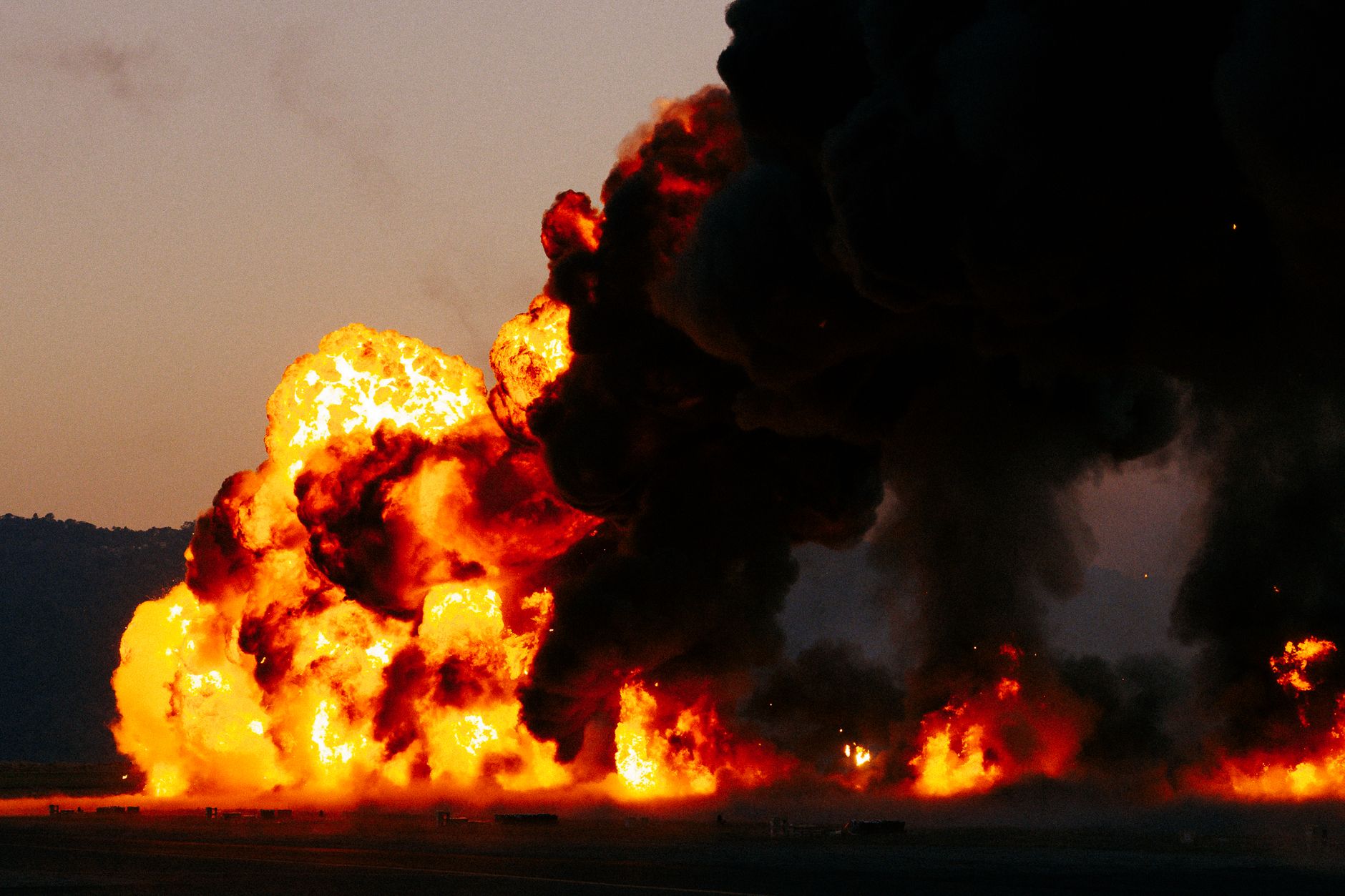 Intense explosion with bright flames and dark smoke filling the sky during twilight.