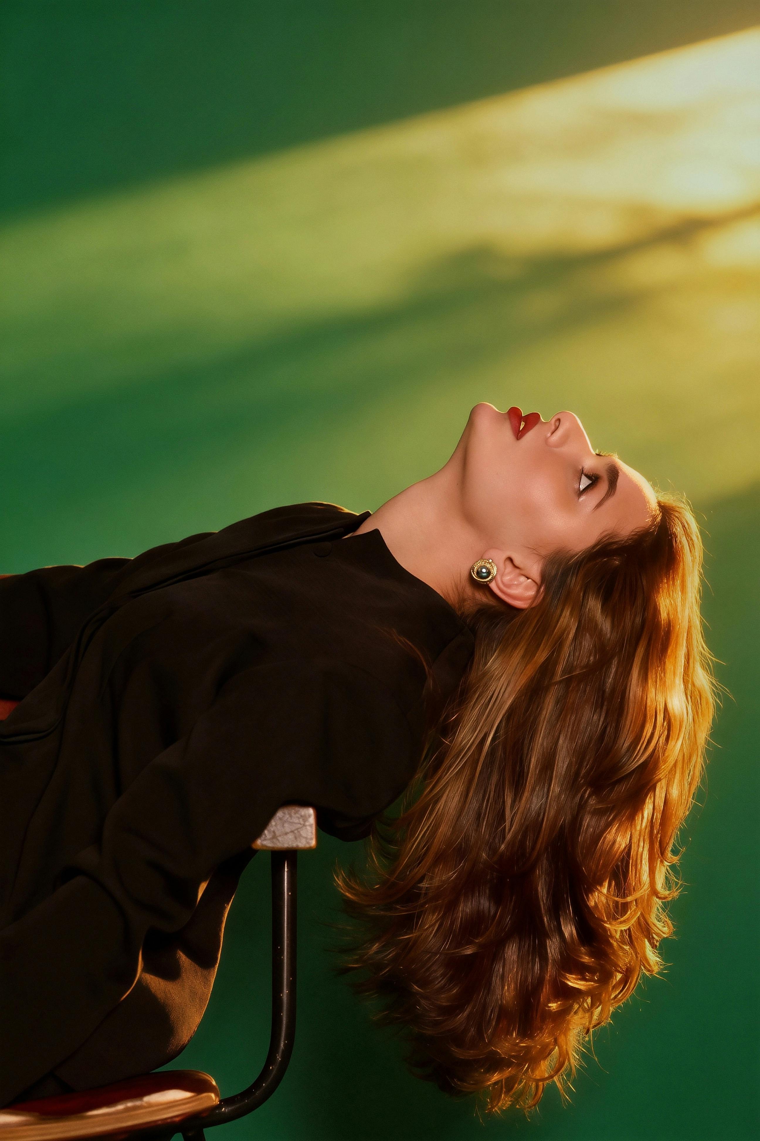 Stylish woman with long hair poses in dramatic lighting against a green background.