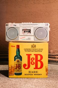 Vintage boombox atop J&B Scotch whisky box in a warm, rustic environment.