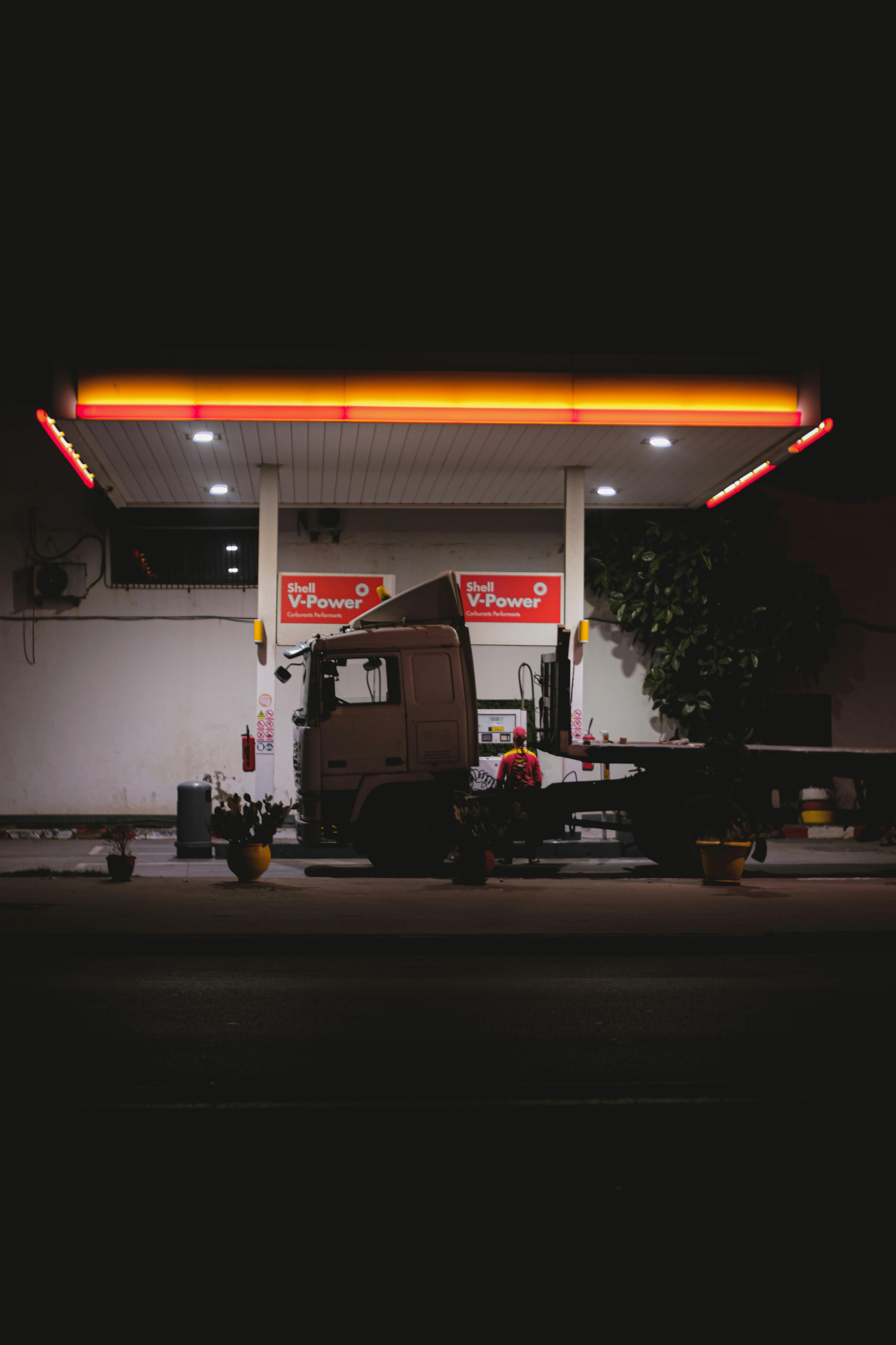 Gratis Un camion solitario è parcheggiato in una stazione di servizio illuminata durante la notte, creando una scena suggestiva e drammatica. Foto a disposizione