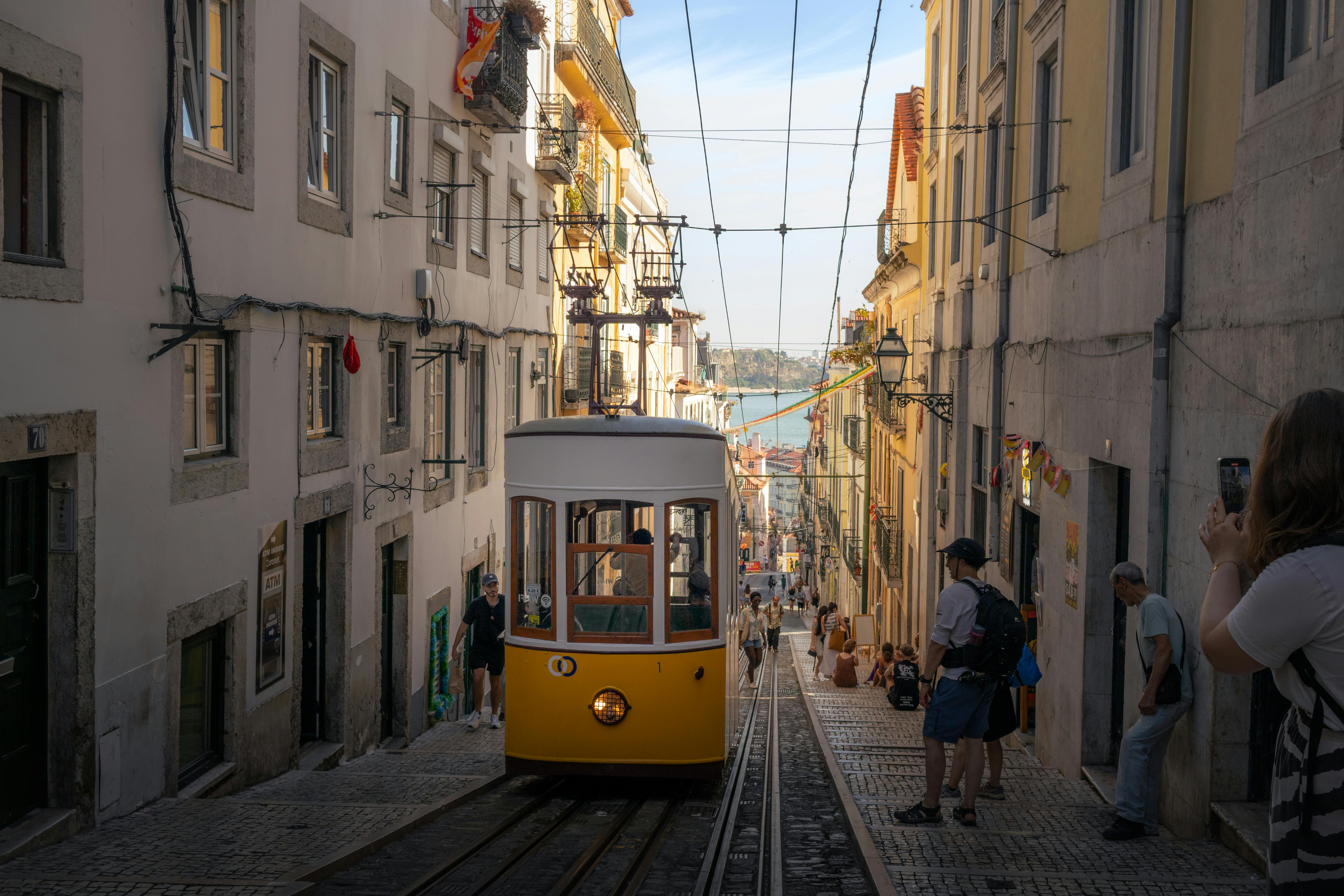 A classic yellow tram navigates a steep street in Lisbon, Portugal, capturing the city's historic charm.