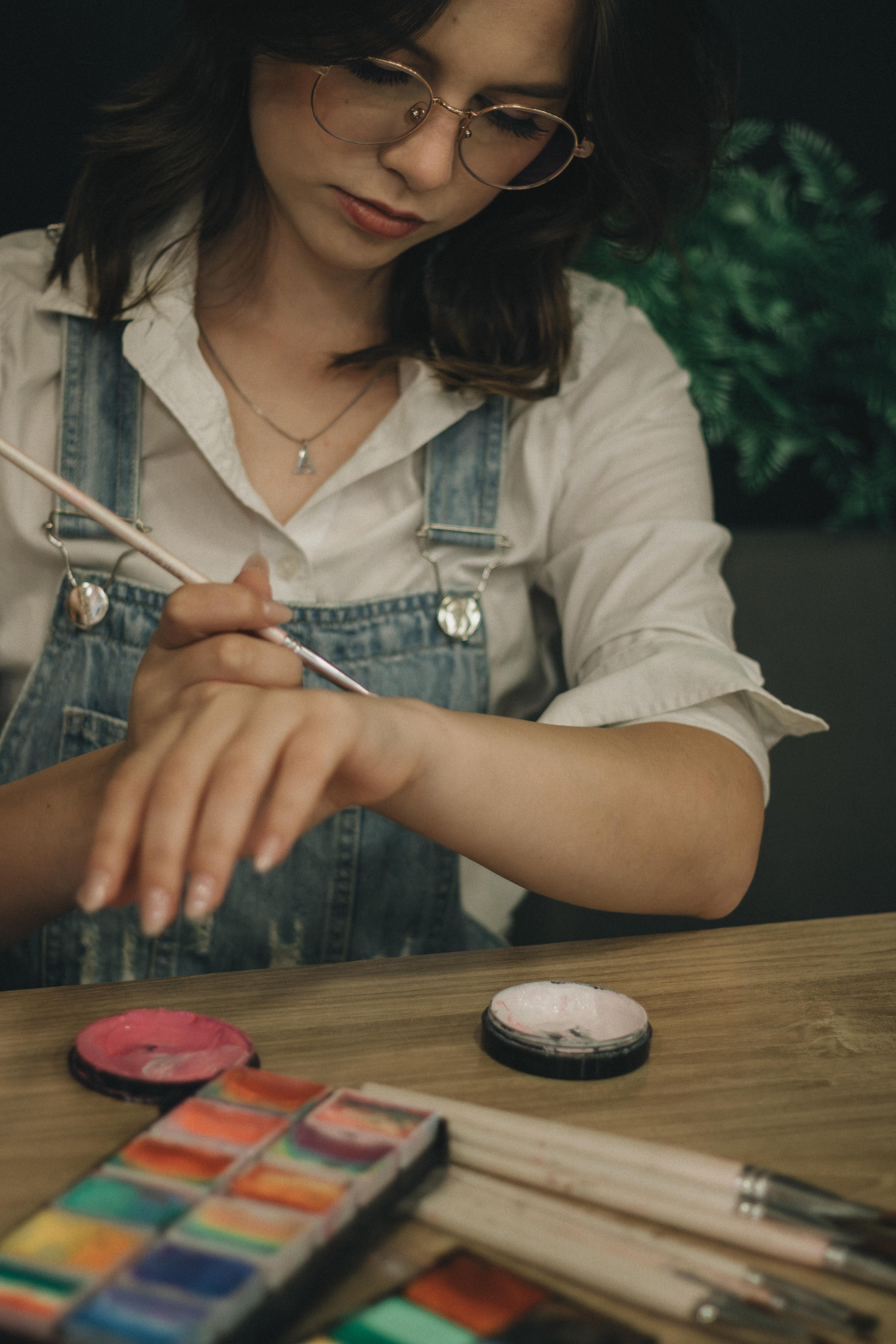Gratis Giovane donna con gli occhiali che dipinge con gli acquerelli. Attività artistica in casa. Foto a disposizione