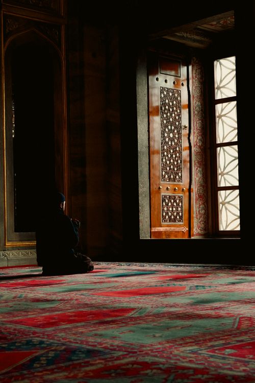 Free Person sitting in prayer inside a beautifully adorned mosque with intricate patterns and warm lighting. Stock Photo