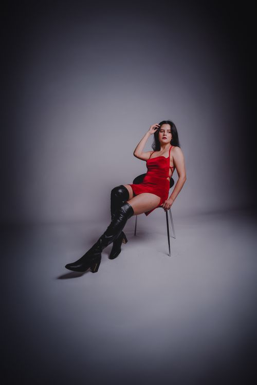 Free Fashionable woman in a red dress and boots sitting on a chair indoors. Stock Photo