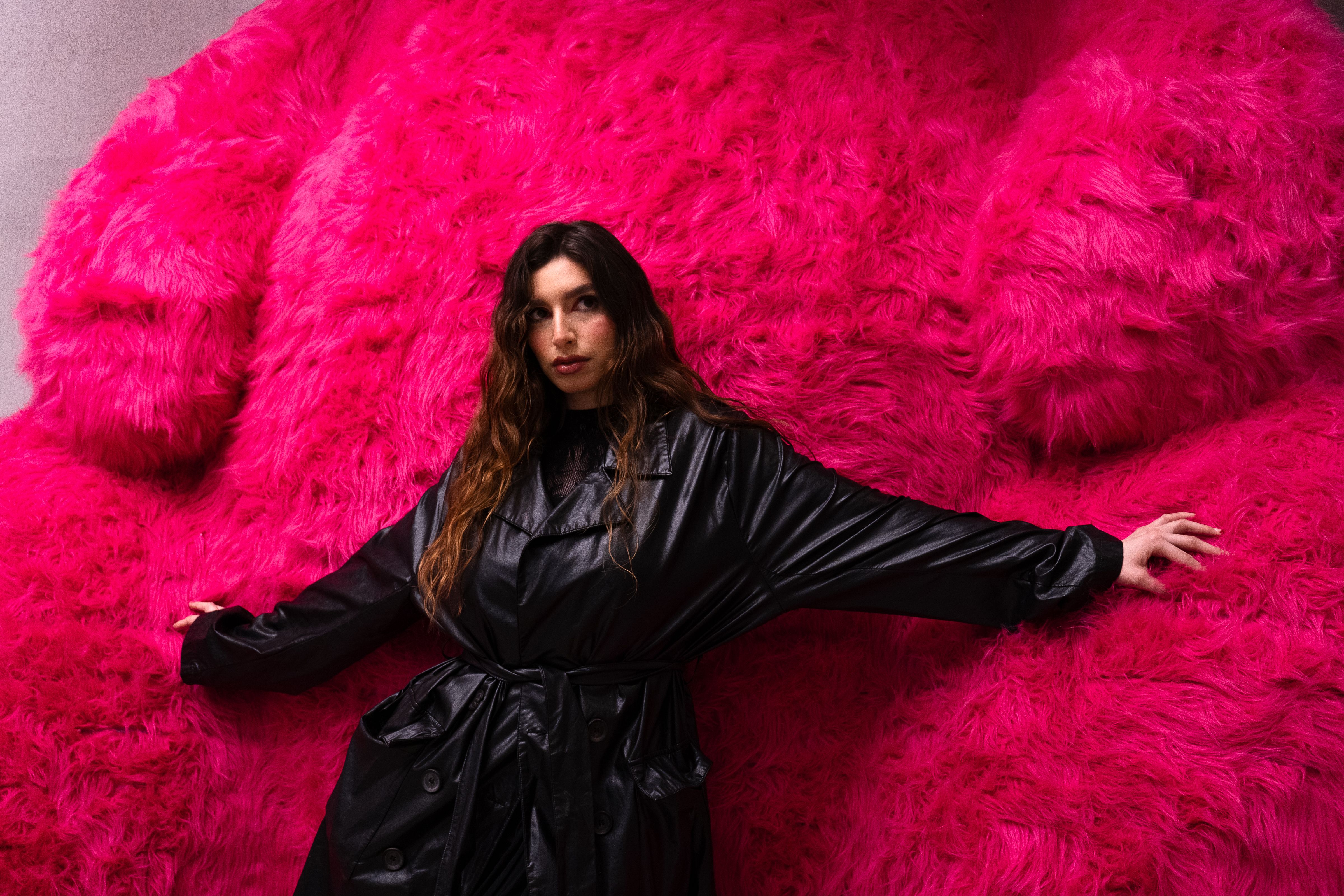 Stylish woman in black coat posing against a vivid pink furry background in Mexico City.