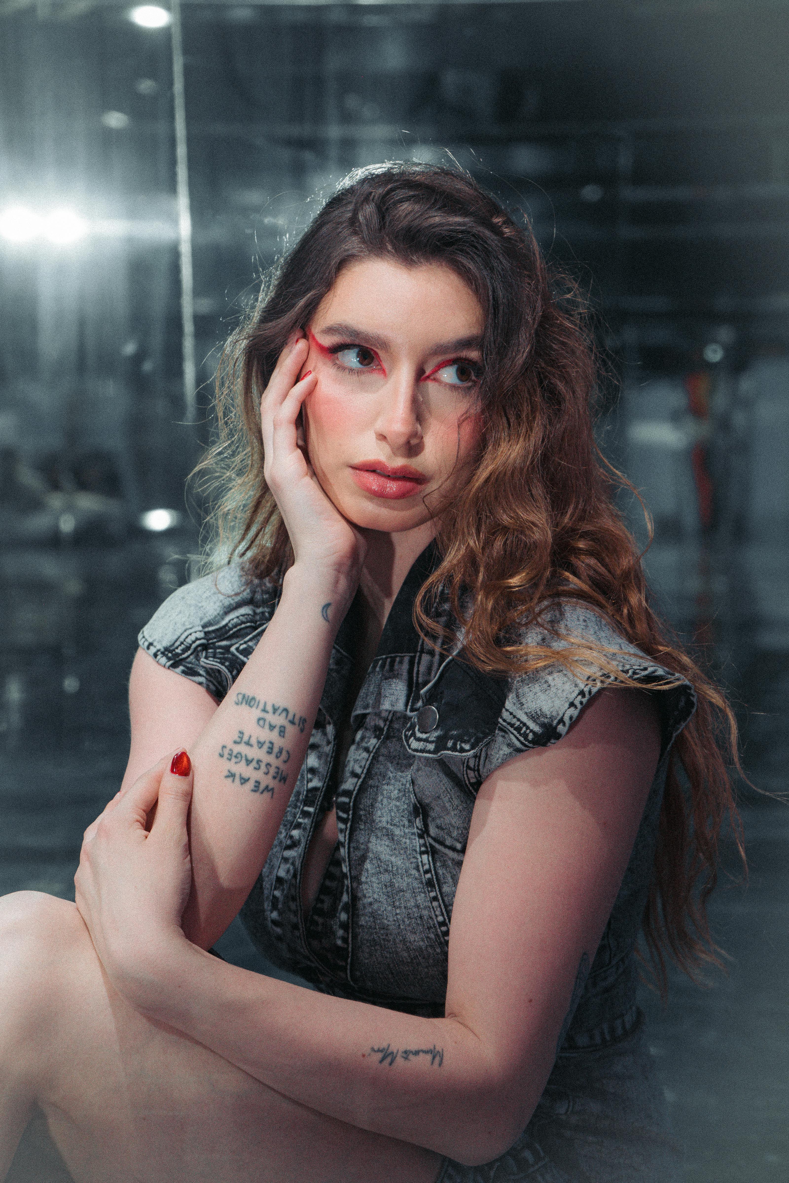 Gratuit Portret artistic al unei femei cu tatuaje, într-o ținută elegantă din denim, pe un fundal reflectorizant. Fotografie de stoc