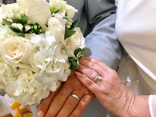 Free A close-up of newlyweds' hands with rings, holding a white floral bouquet, symbolizing love and commitment. Stock Photo