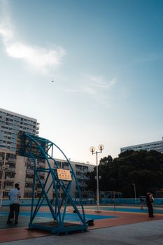 A serene evening at a basketball court in Kowloon, Hong Kong, with high-rise buildings in the background.