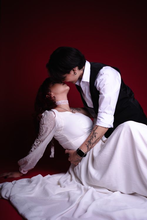 Free An intimate moment between a couple dressed in elegant white attire against a red backdrop. Stock Photo