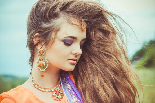 Free Close-up portrait of a woman with flowing hair, wearing traditional jewelry outdoors. Stock Photo