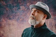 一位戴着软毡帽、留着胡须的老人特写肖像，背景是丰富的纹理