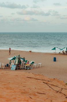 Relaxing sandy beach scene in RN Brazil with people and umbrellas under a partly cloudy sky.
