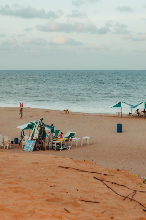 Free Relaxing sandy beach scene in RN Brazil with people and umbrellas under a partly cloudy sky. Stock Photo