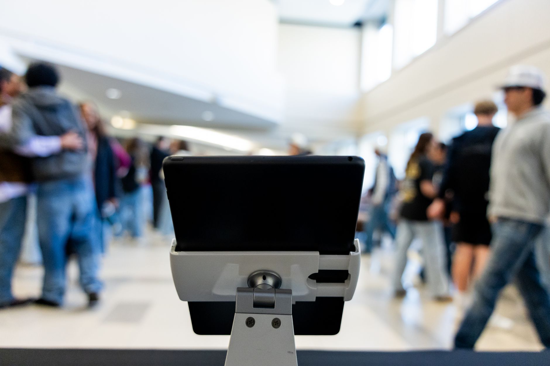 A close-up of a tablet in an indoor public setting, with blurred people in the background.