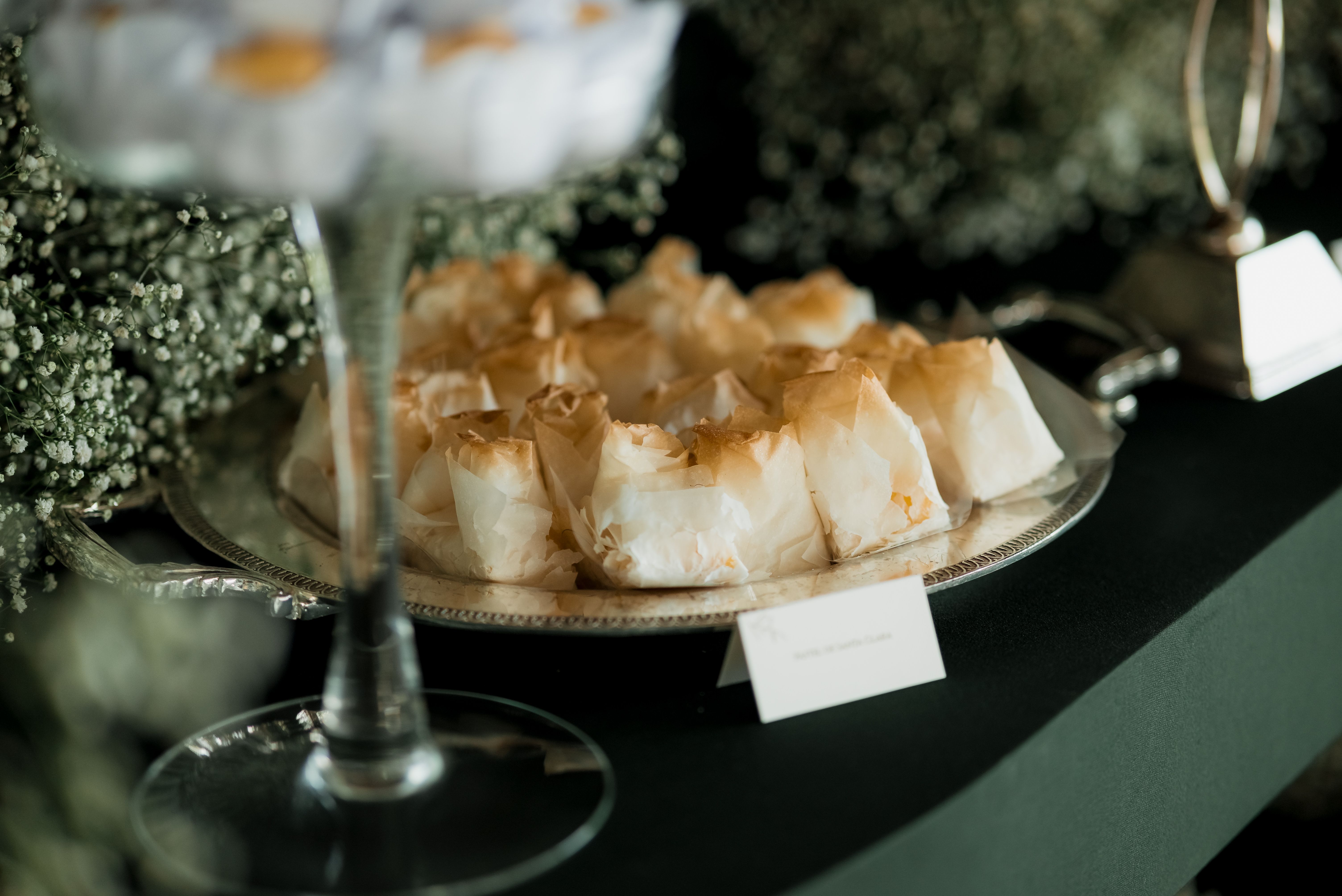 Delicate pastries elegantly arranged on a silver tray surrounded by lush greenery. Ideal for catering and event themes.