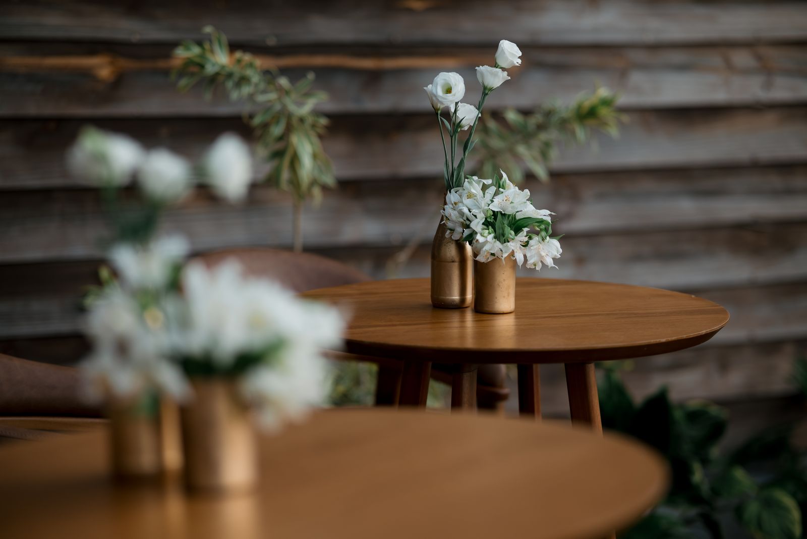 Elegant outdoor cafe setting with wooden tables and floral centerpieces in gold vases, perfect for rustic decor inspirat