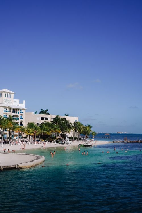 Free Relaxing beach view in Cancún with clear blue waters and palm trees. Stock Photo