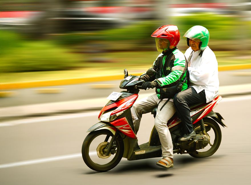 A motorcycle carrying two people speeding through a city street with blurred motion effect.