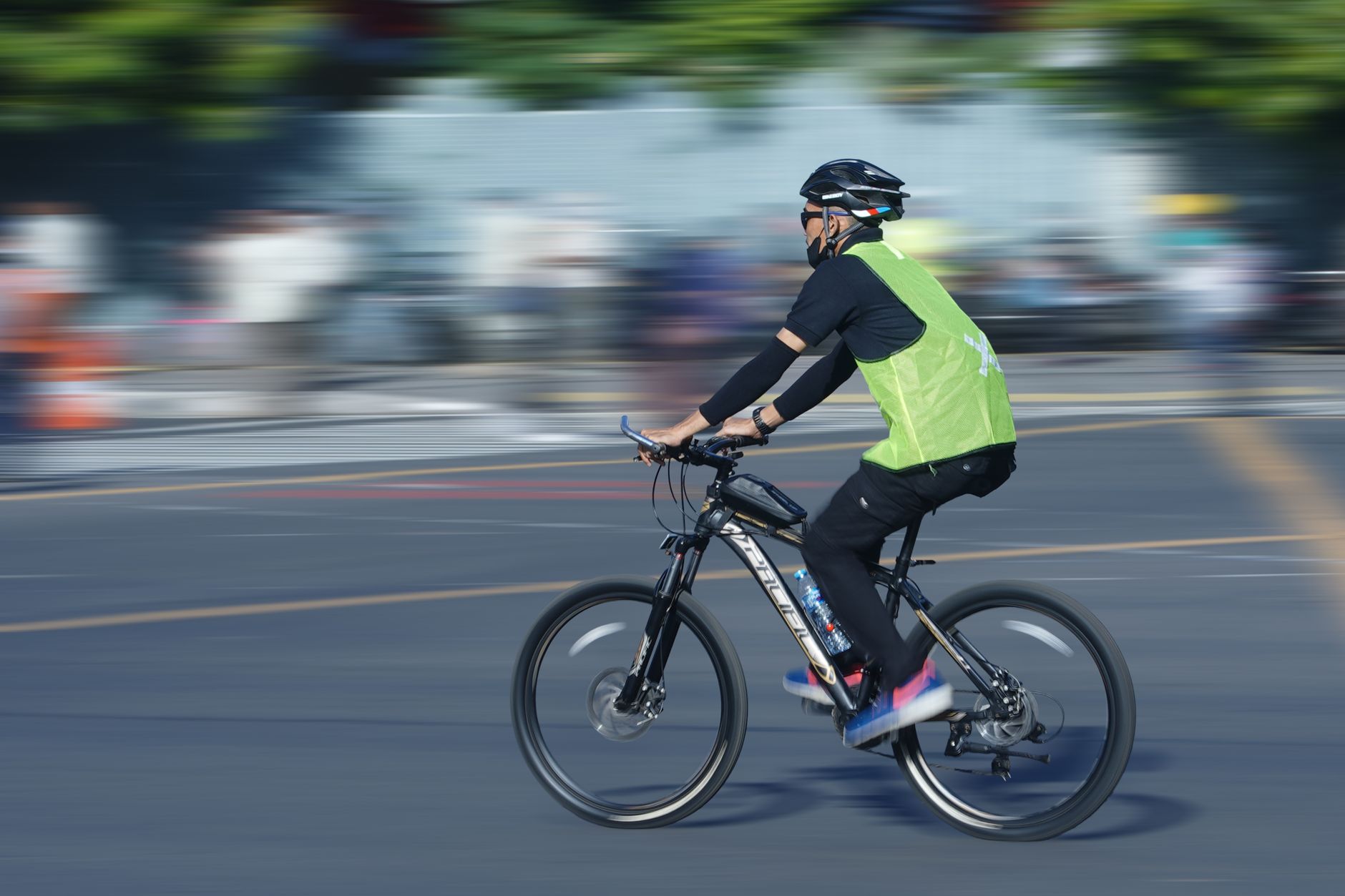 A cyclist wearing safety gear rides swiftly through an urban area, showcasing motion and speed.