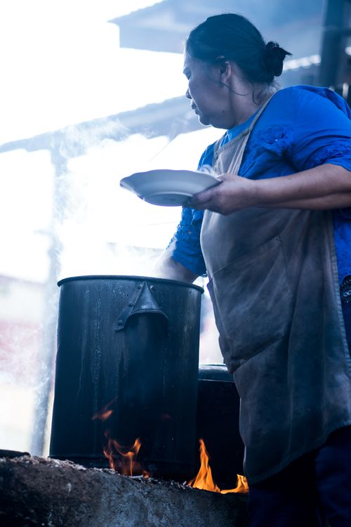 Free A woman in a blue shirt and apron preparing food over an open flame outdoor. Stock Photo