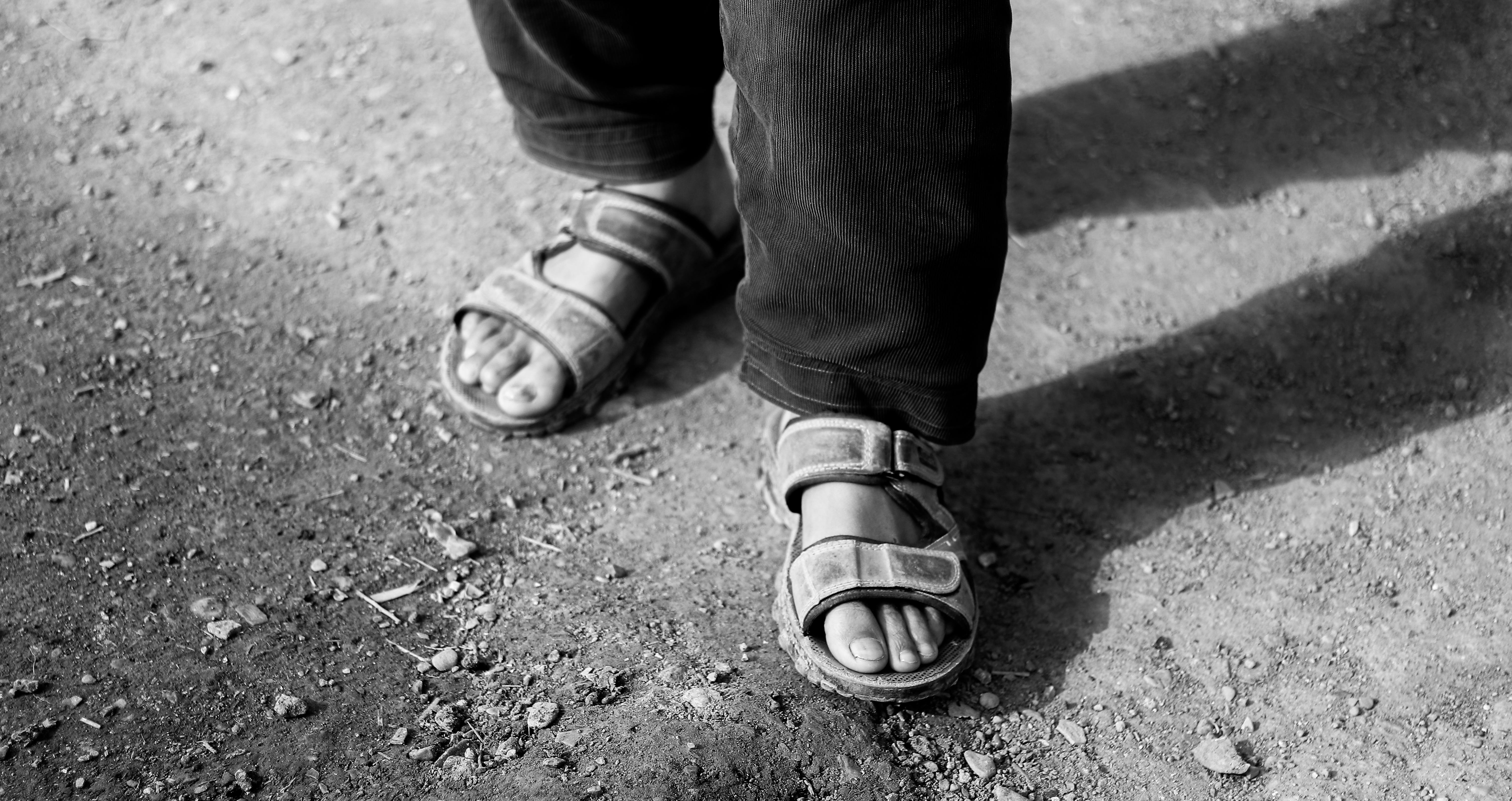 grátis Close-up de sandálias em um caminho empoeirado, projetando uma sombra, em preto e branco. Foto profissional